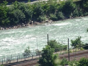 Flussufer mit Gleisen und Radfahrer.