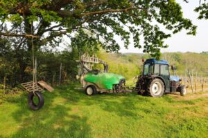 Traktor und Sprühgerät auf grüner Wiese bei Bäumen.