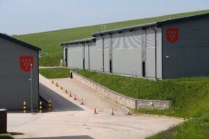 Industriegebäude mit roten Wappenschildern auf grüner Wiese.
